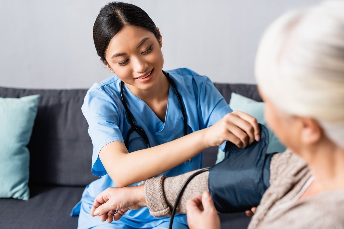 A female nurse fixing the tonometer cuff on an elderly patient.
