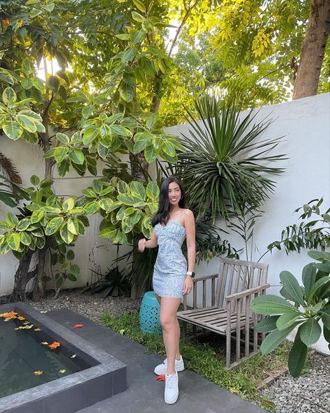 A woman wearing a blue spaghetti strap summer dress and white sneakers. 