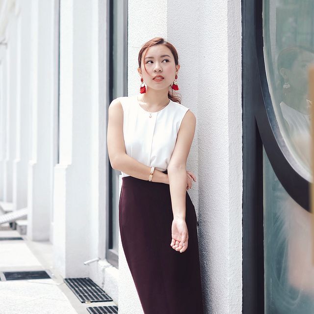 A woman wearing a white sleeveless top and maroon maxi skirt.
