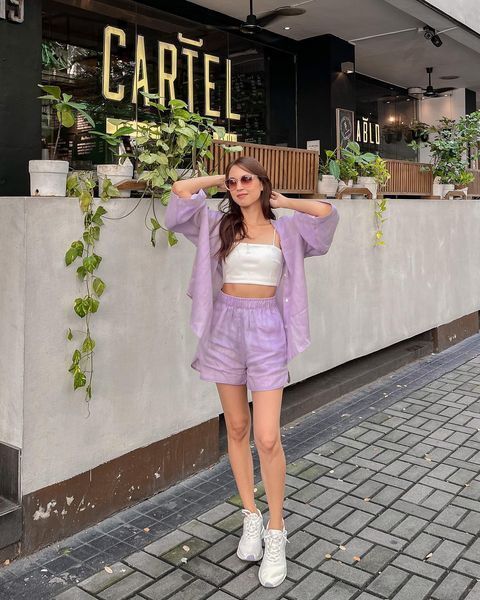 A woman wearing a matching purple shirt and shorts with a pair of white trainers.