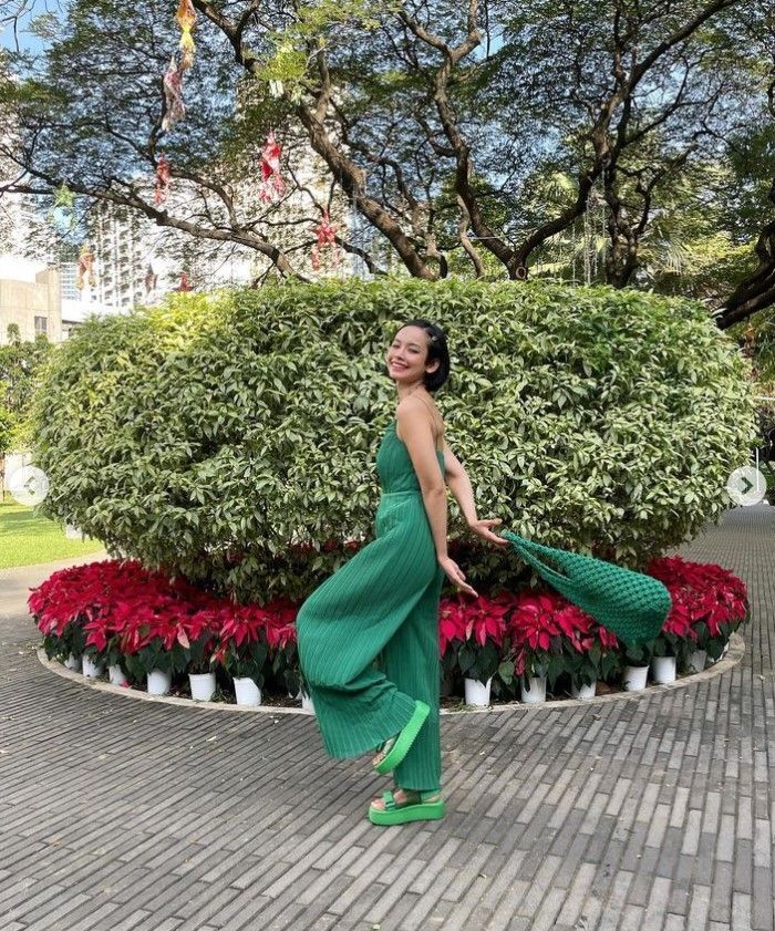A woman wearing a green jumpsuit with green platform sandals and a green tote bag.