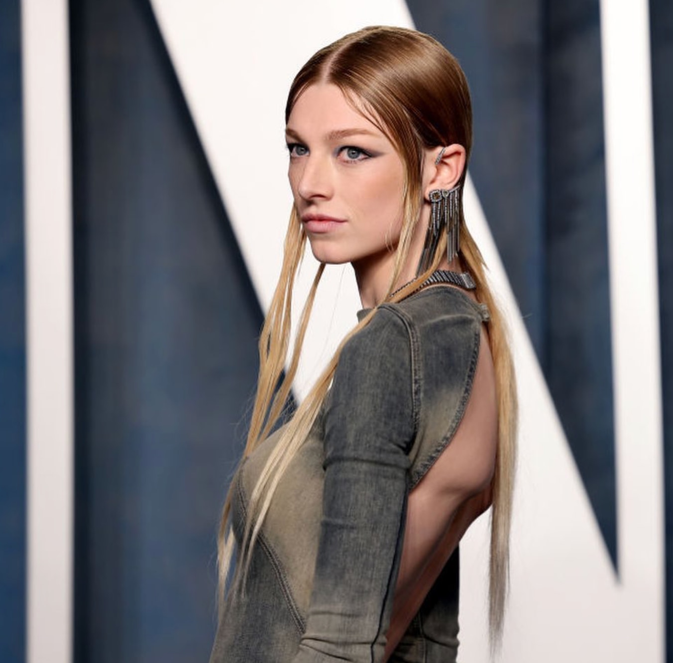 Hunter Schafer with long hair posing in a dark denim dress.