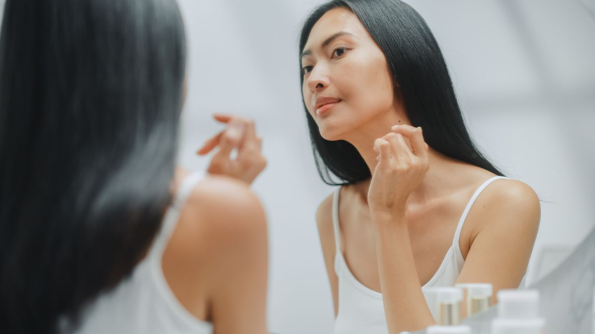 Asian woman is checking her face in the mirror.