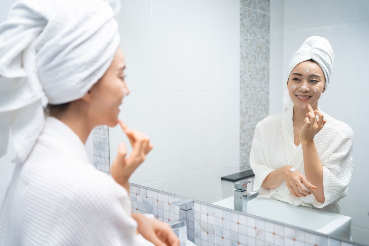 Asian woman applying skin care in front of a mirror