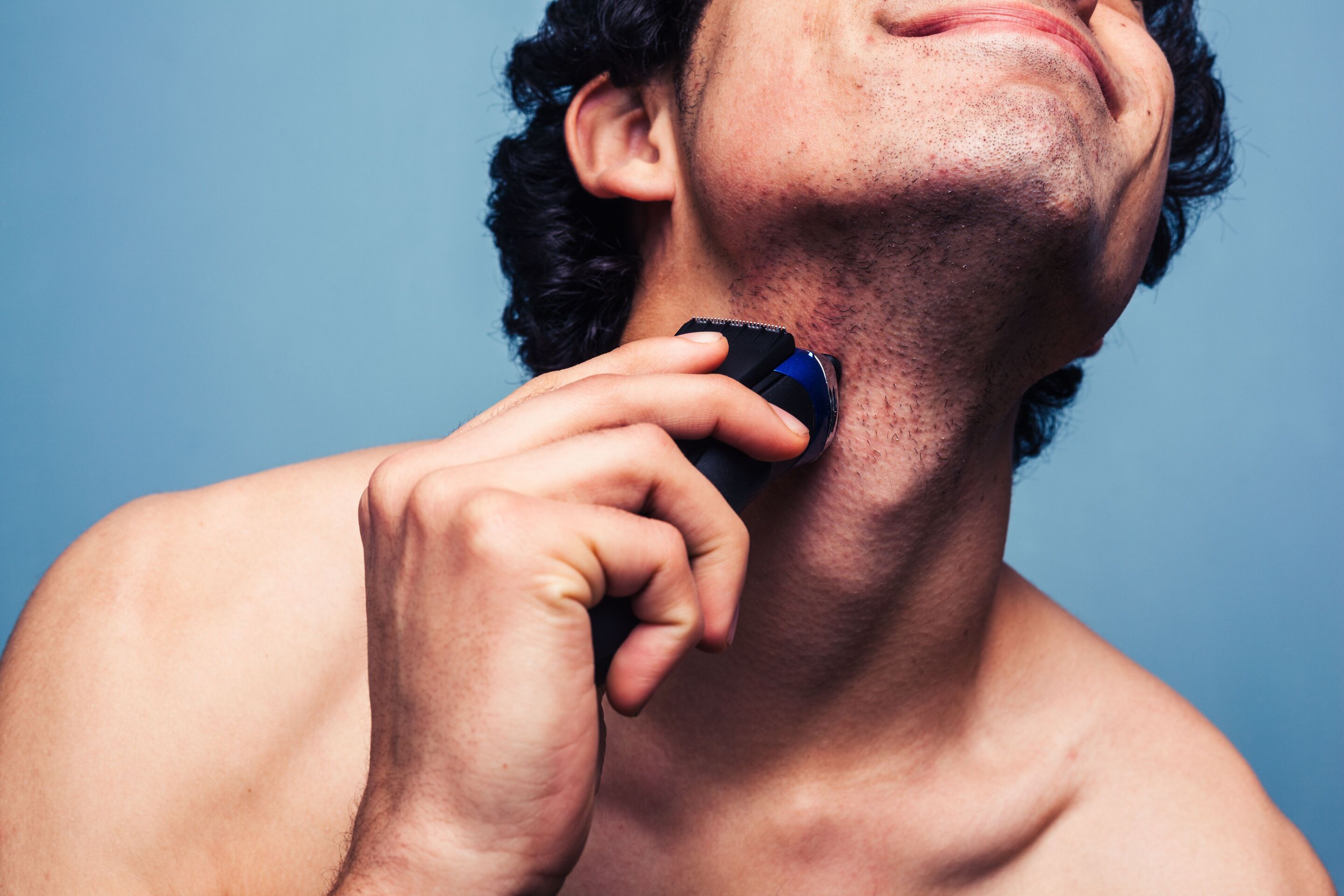 A close up shot of an Asian man shaving his beard with an electric razor