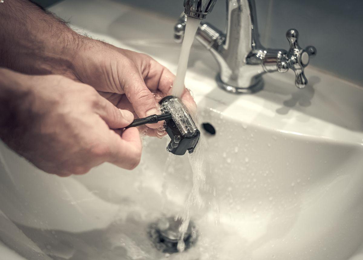 A man rinses a shaving razor in a bathroom sink. 