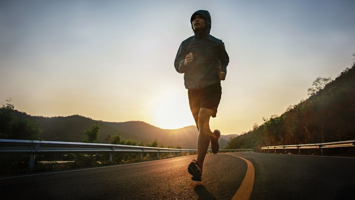 A man jogs down a road while the sun rises. 