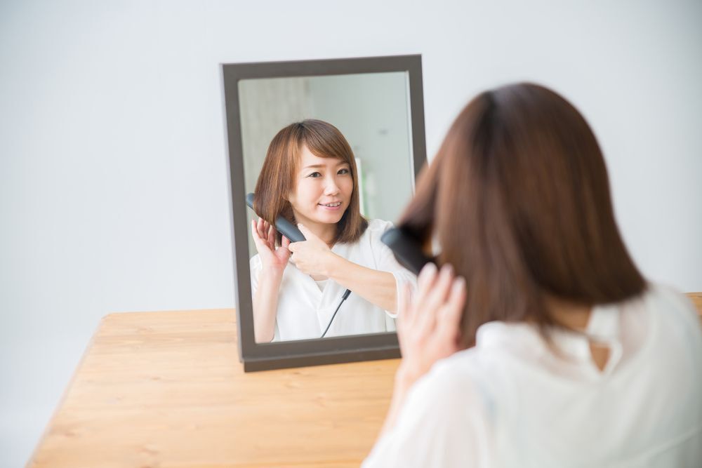 An Asian woman ironing her hair.