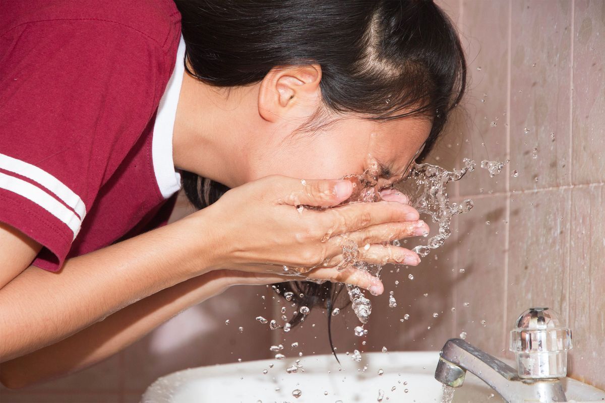 Filipino woman in a maroon shirt rinsing her face with water.