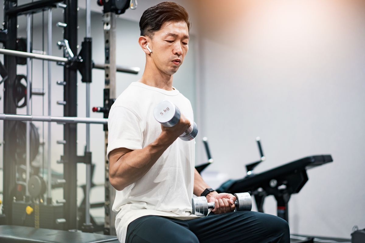 Man wearing Airpods lifting dumbbells in a gym.