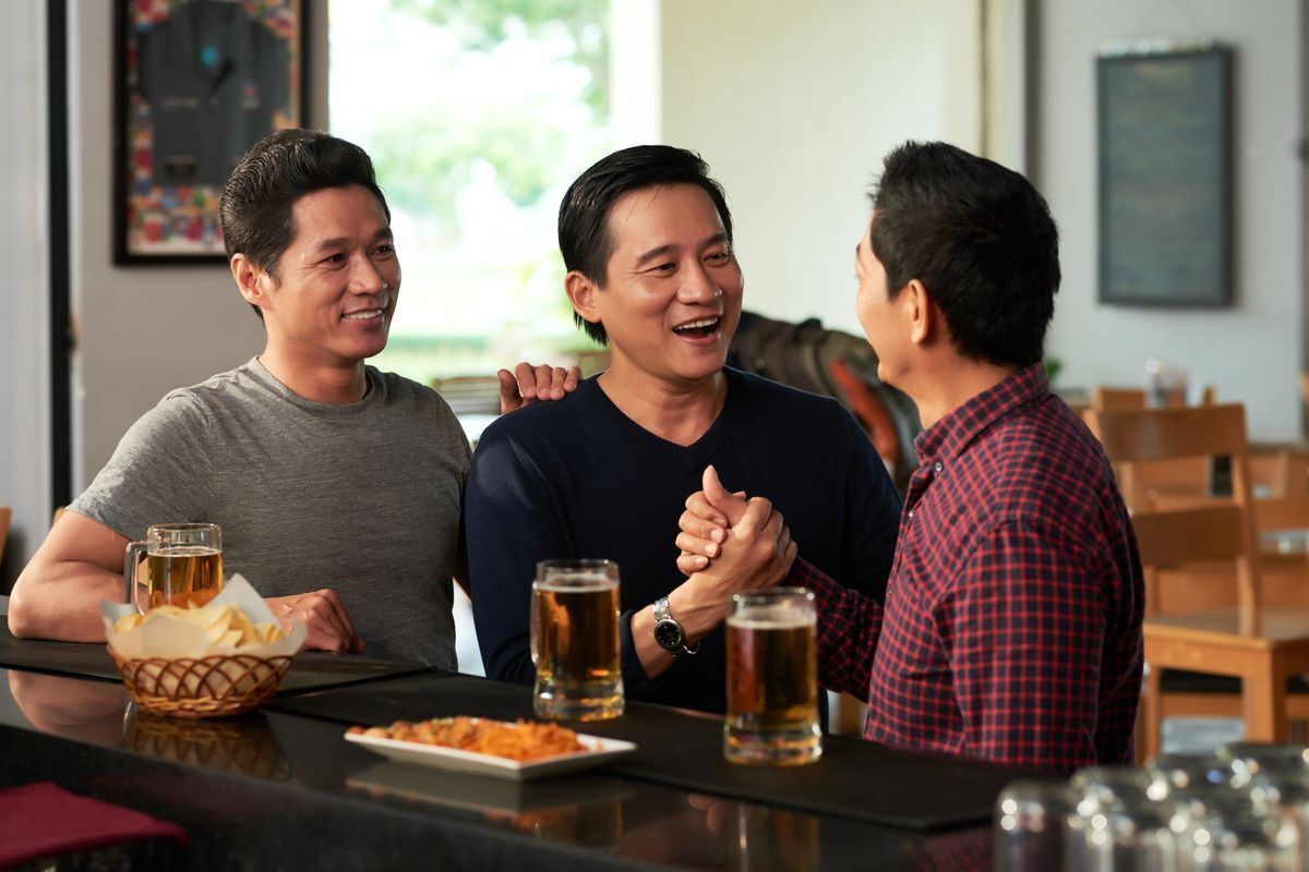 Three men hanging out together at a bar, drinking beers.
