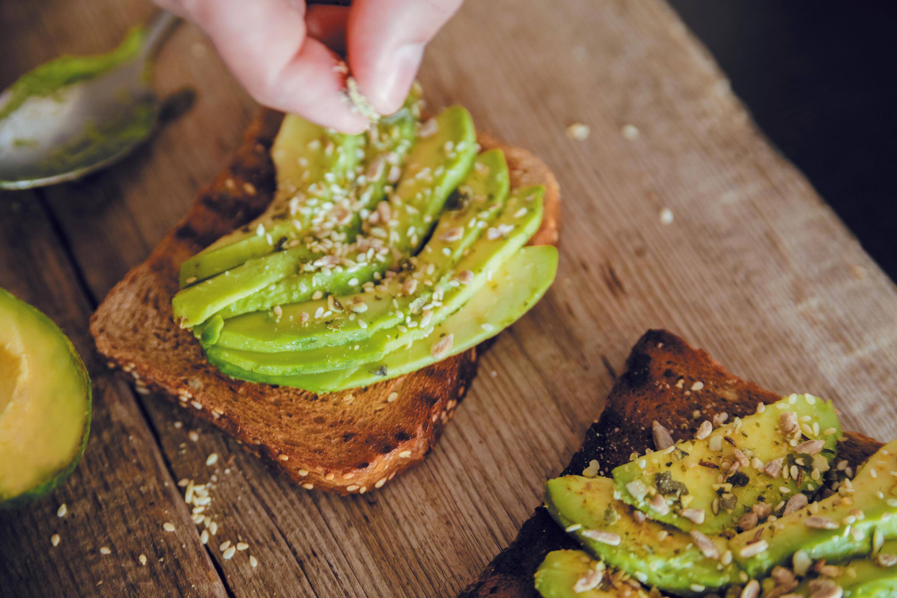 Hand sprinkling seeds on avocado toast