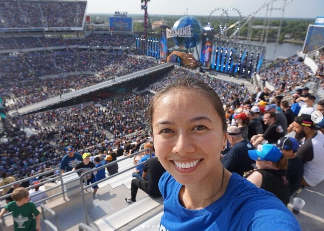 Asian woman in a blue shirt taking a selfie in a crowded arena.