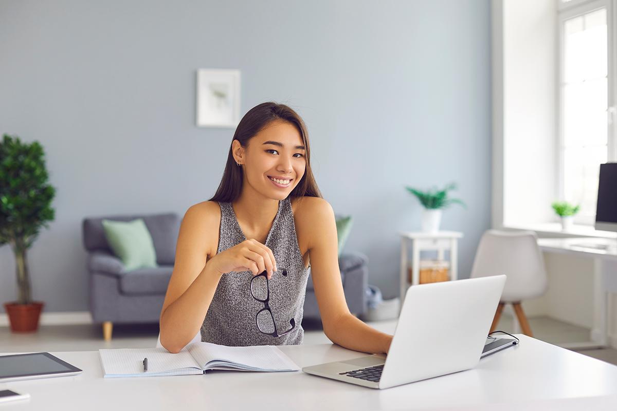 Asian woman in gray sleeveless top in front of laptop while holding glasses