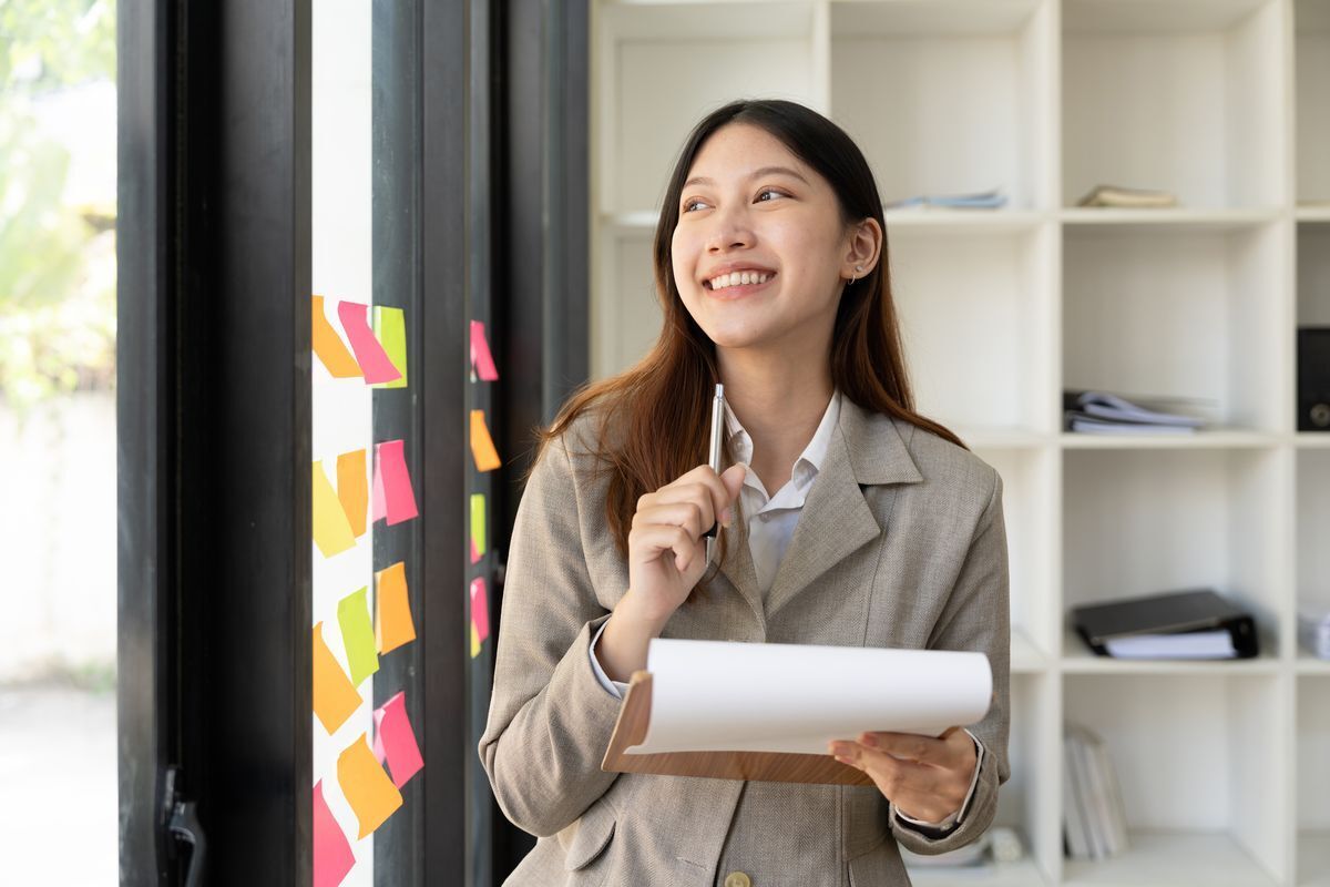 Asian woman holding clipboard and pen and looking outside