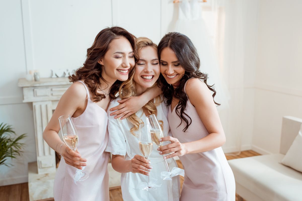 Three Asian women holding champagne glasses and embracing while smiling