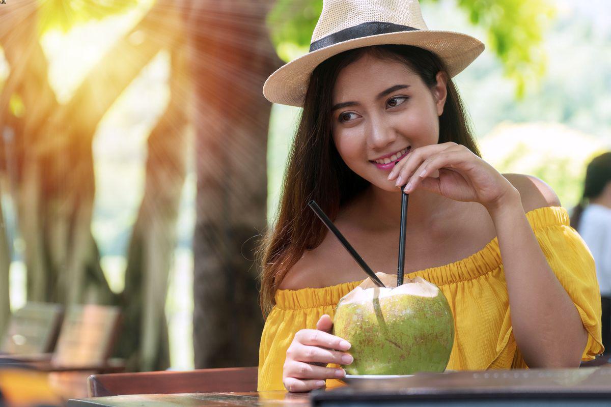 Asian girl with hat drinking coconut at the beach 