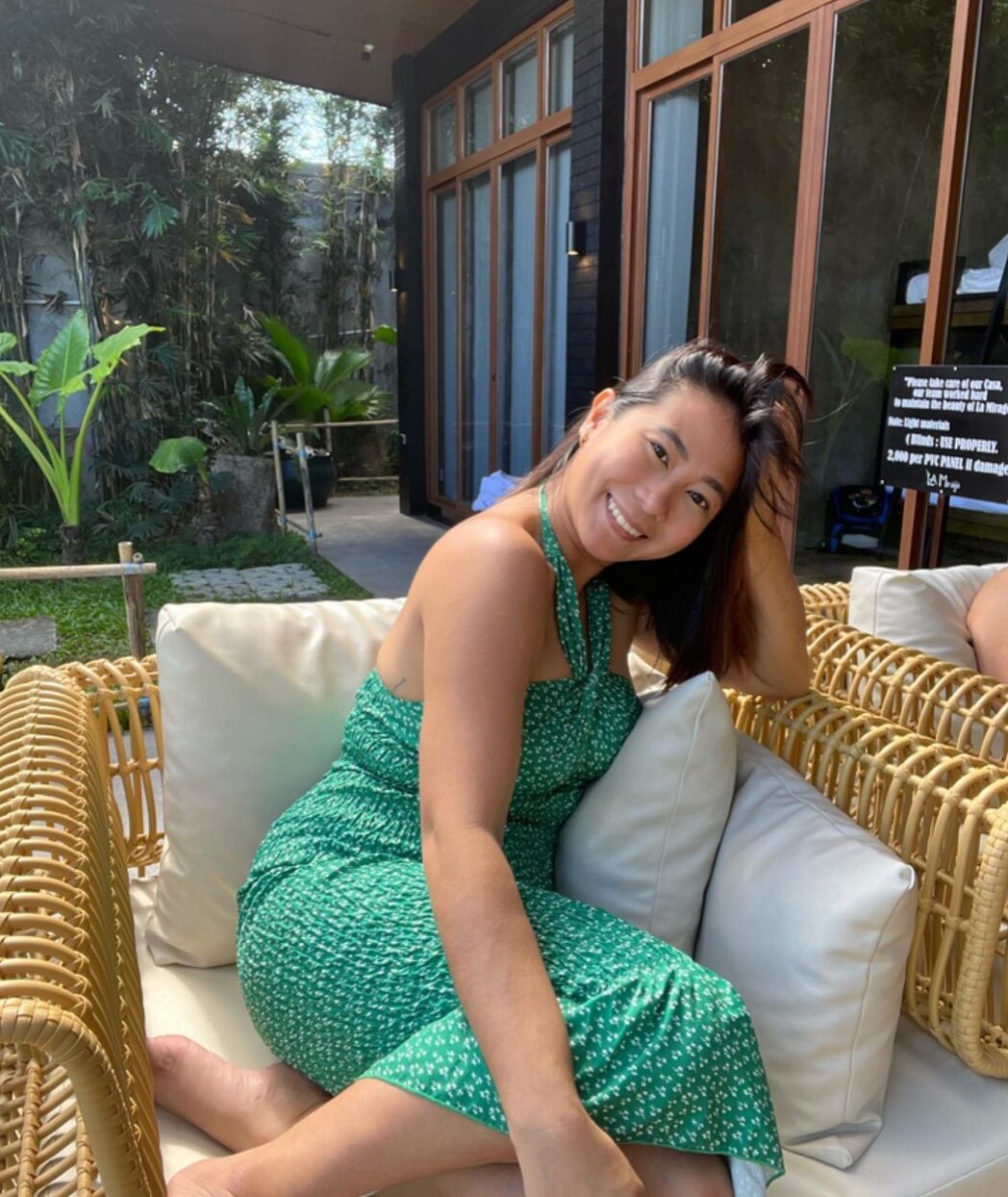 Smiling Asian woman in a green dress seated on a lounge chair. 