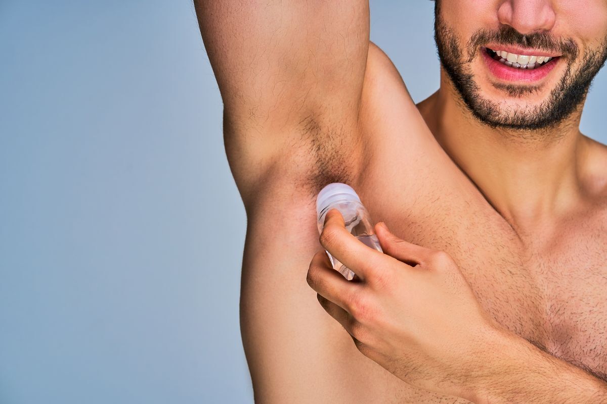 Fit young man applies roll on deodorant.