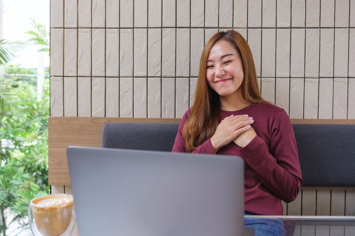 Happy Asian woman holding her hands to her chest while on a video meeting