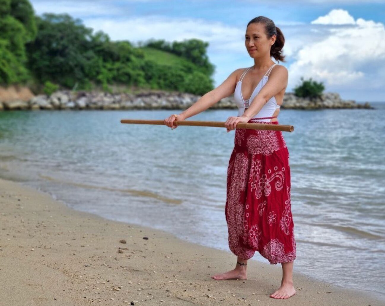 Asian woman holding a bamboo stick on the beach.