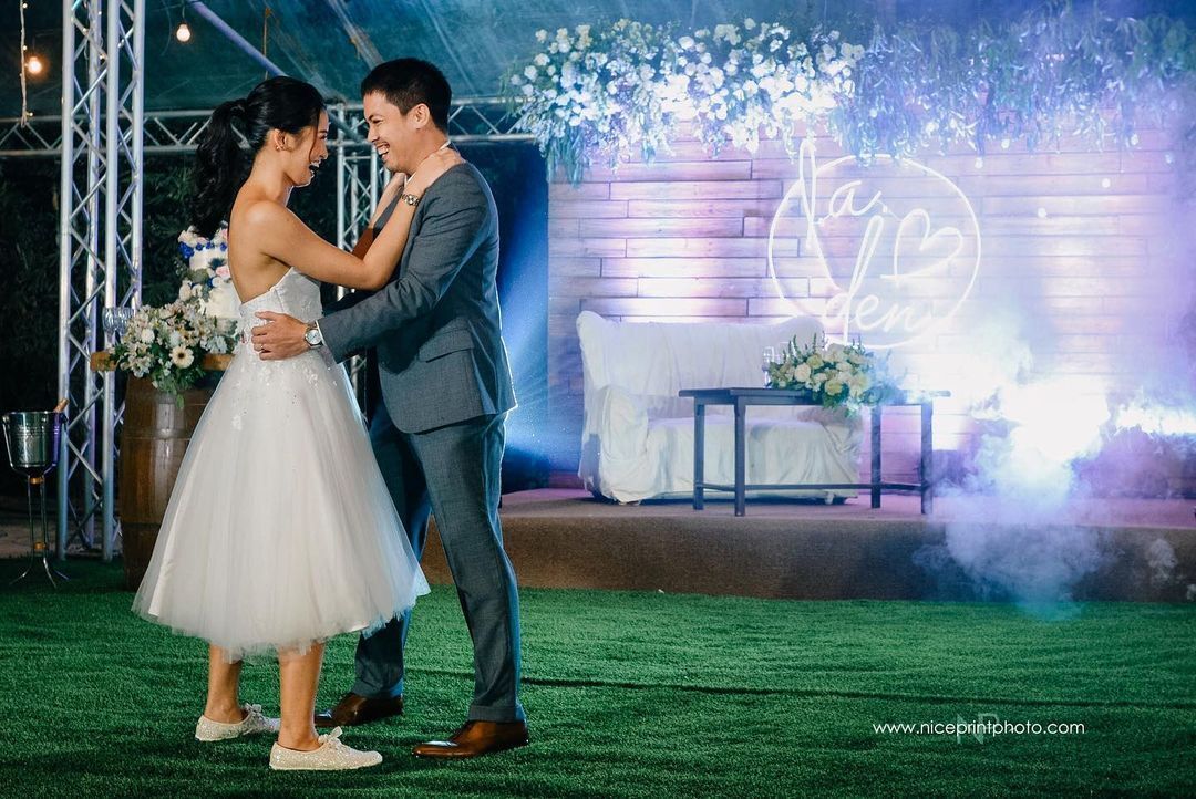 Asian couple dancing during reception with bride wearing sneakers with white dress.