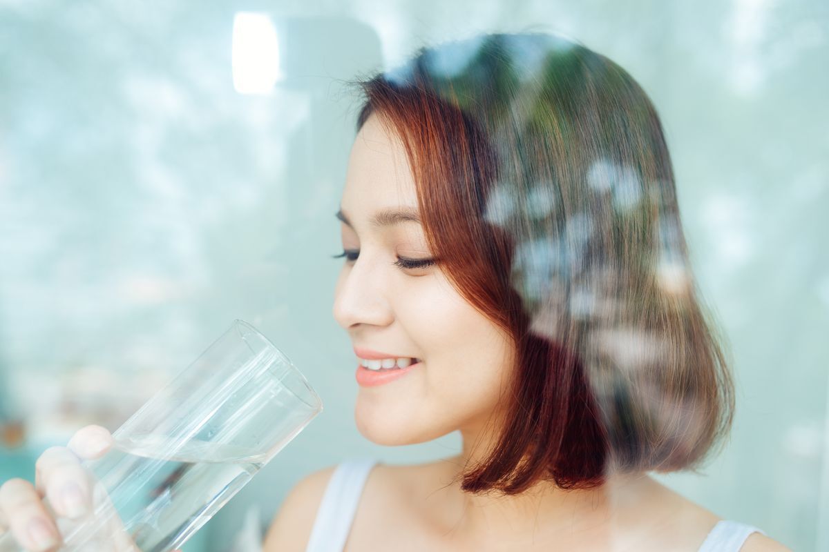 Asian woman holding a glass of water seen behind a glass window.