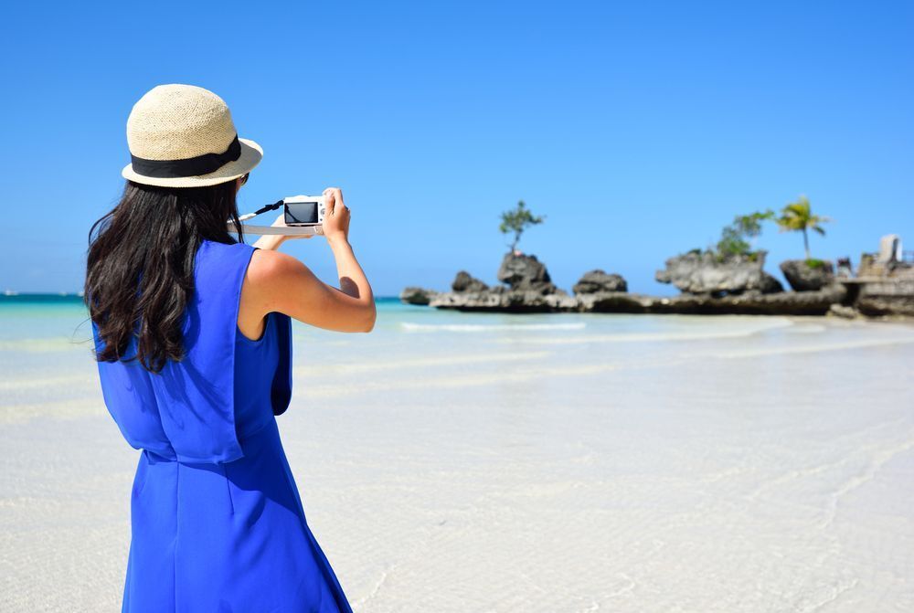 Back of an Asian girl in straw hat and blue dress taking a photo of Willy’s Rock.