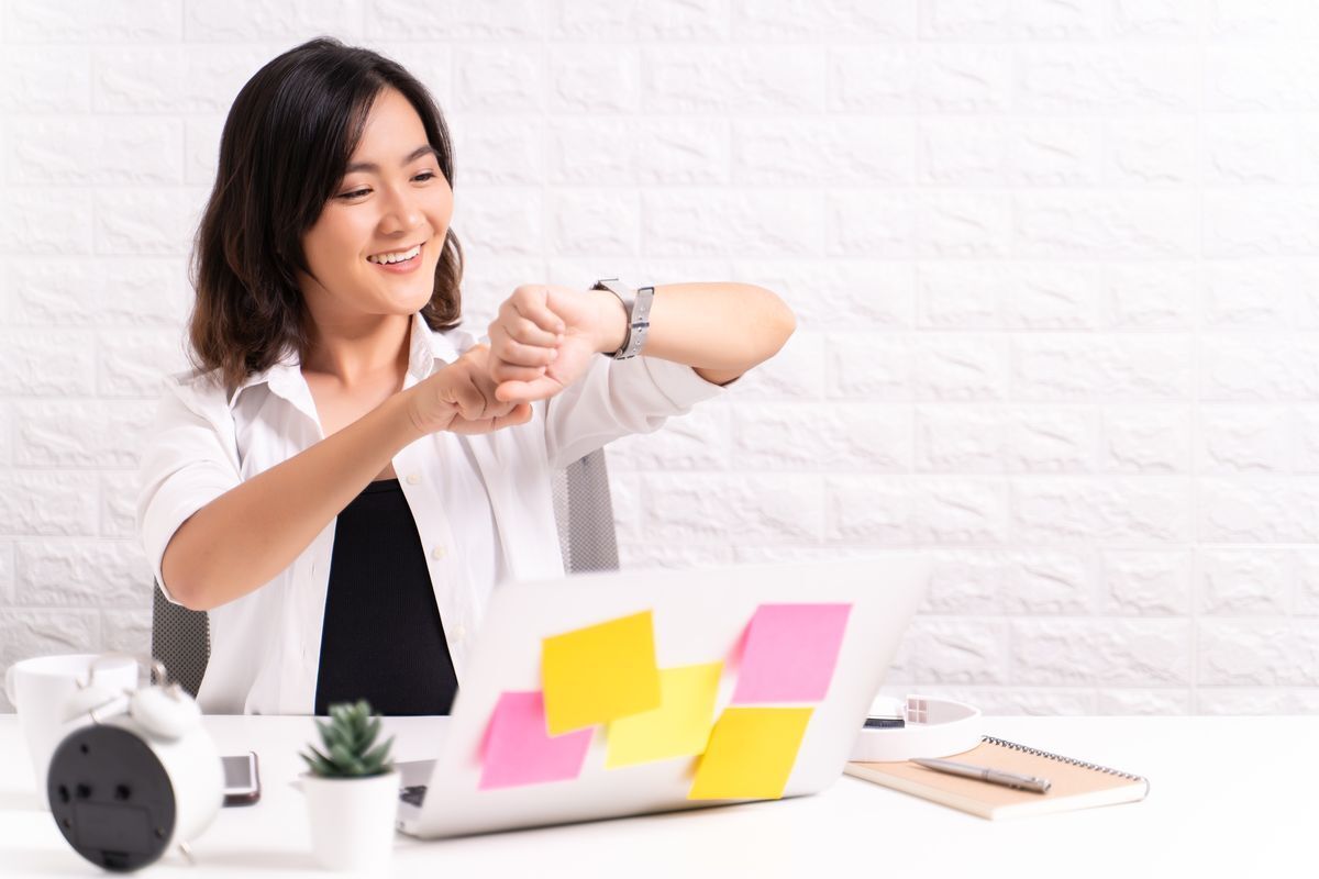 Asian woman checking watch while working in front of a computer