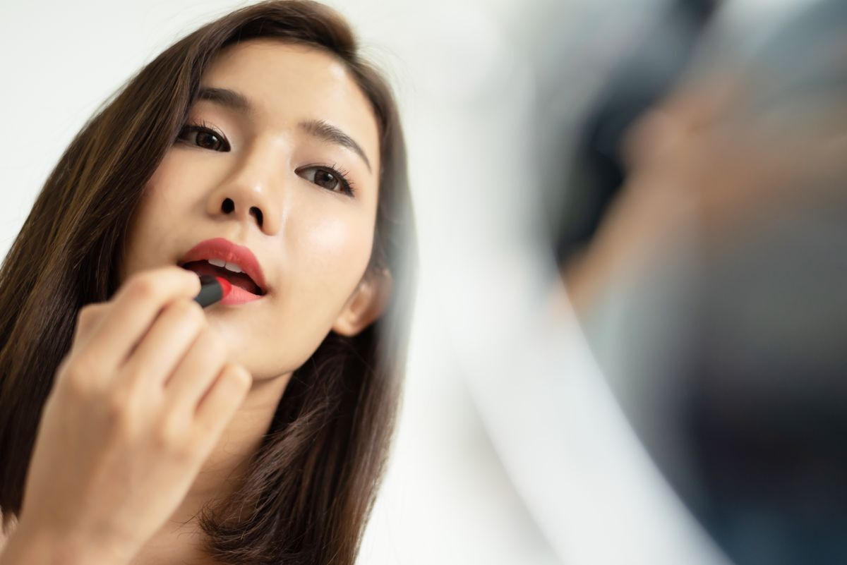Woman applying red lipstick in front of a mirror. 