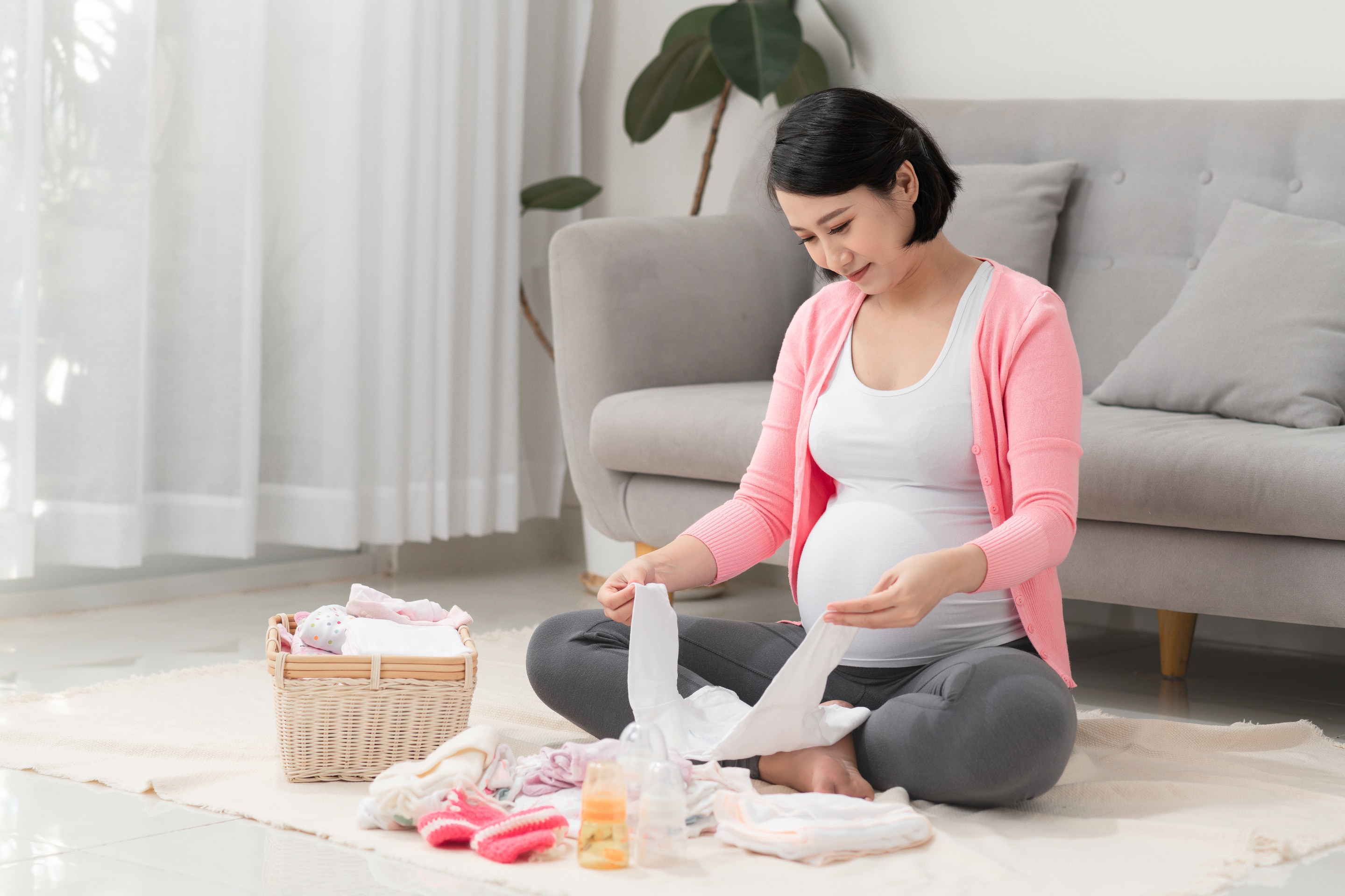 Wanita asia yang sedang hamil mempersiapkan perlengkapan baju bayi
