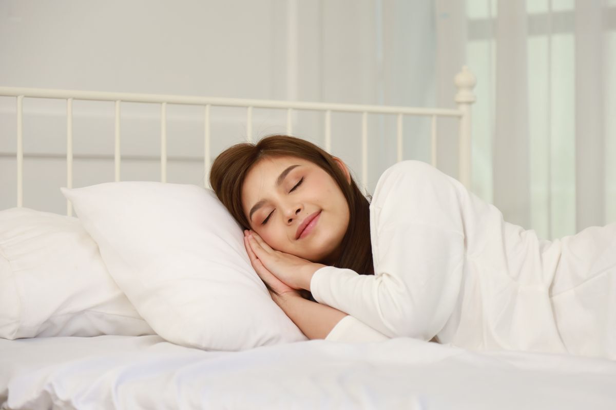 Asian woman wearing a white sweater, sleeping on white sheets.