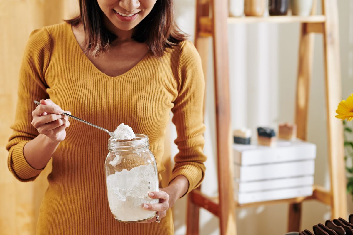 A woman taking a spoonful of baking soda out of a jar.