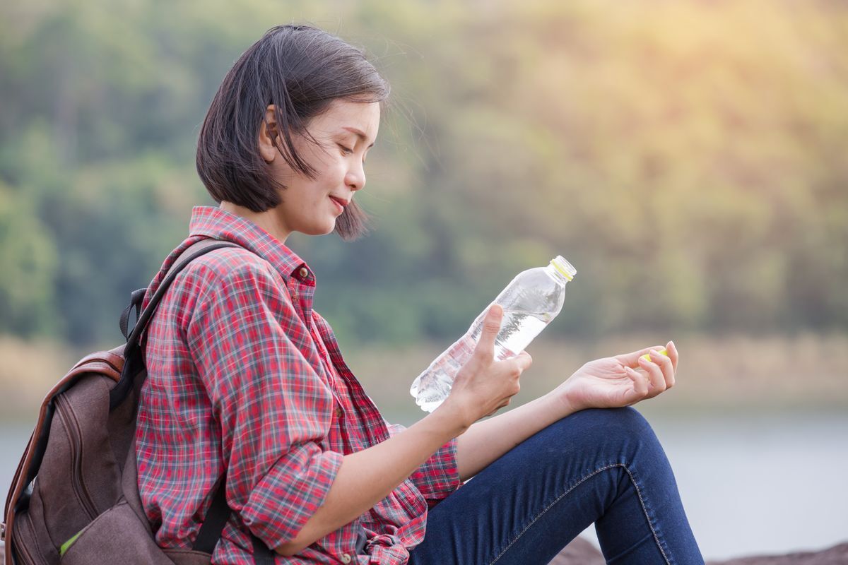 Asian woman sitting on the ground with a backpack, holding bottled water.