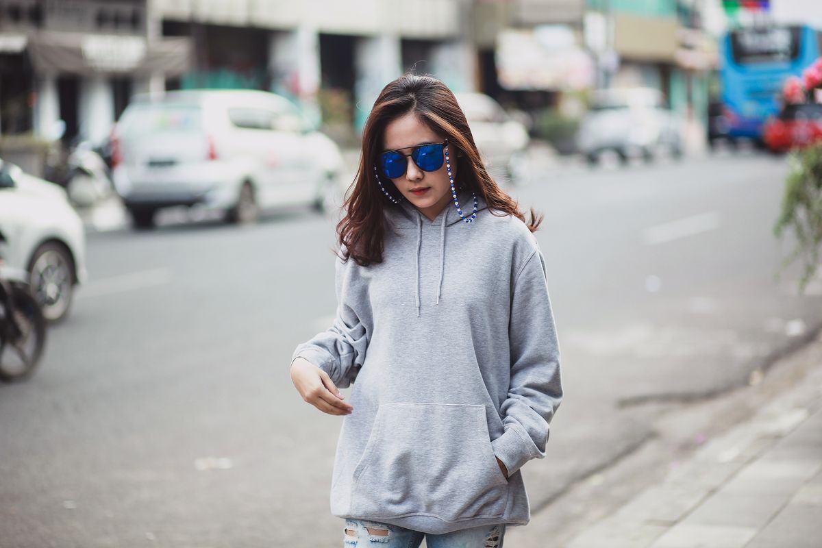 Asian woman wearing a hoodie and sunglasses walking on the street.