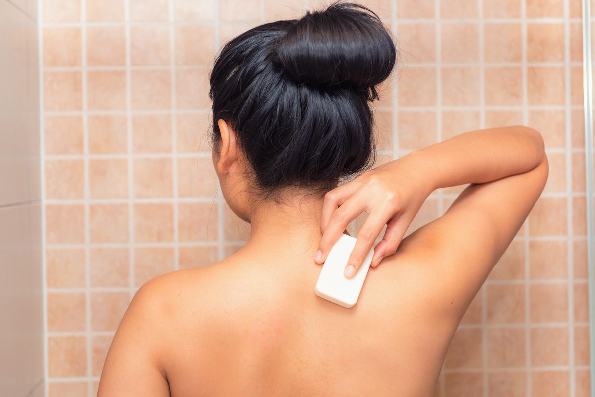 Back of an Asian woman holding a bar of soap in the shower.