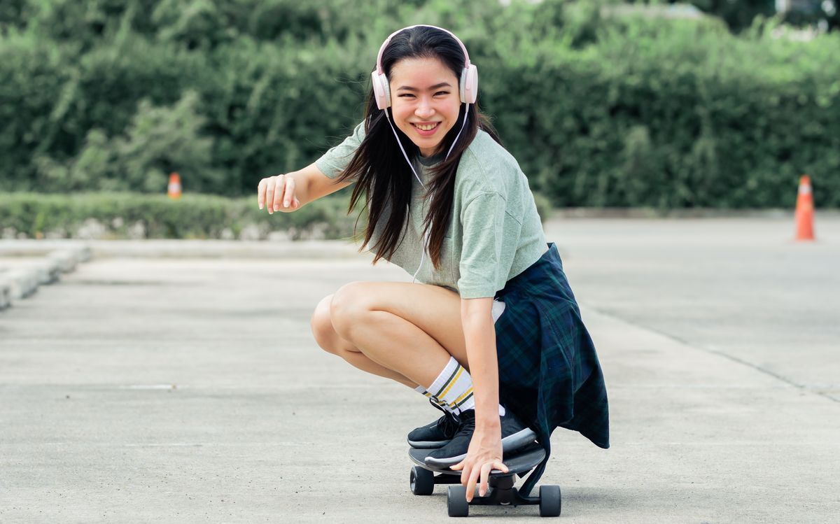 Asian woman wearing shorts and a headset riding a skateboard.