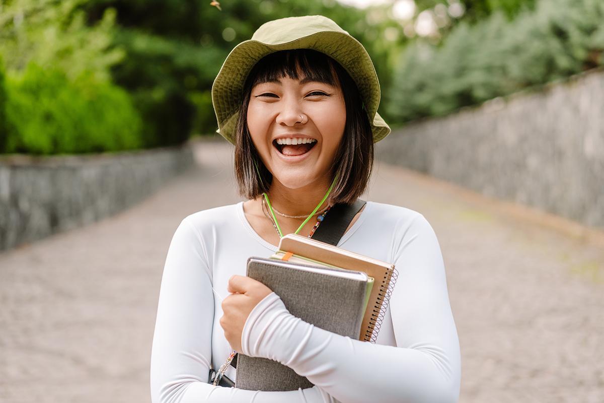 Asian woman wearing a hat and holding notebooks
