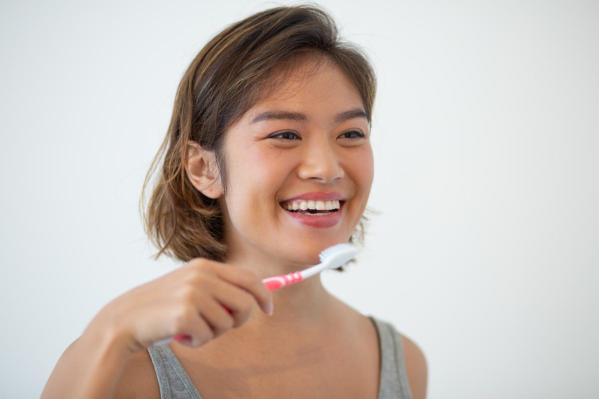 Smiling Asian woman brushing her teeth