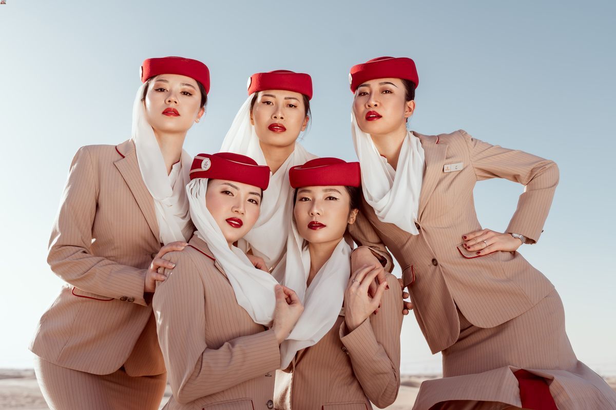 Emirates flight attendants in brown suits and red caps posing in front of the camera.