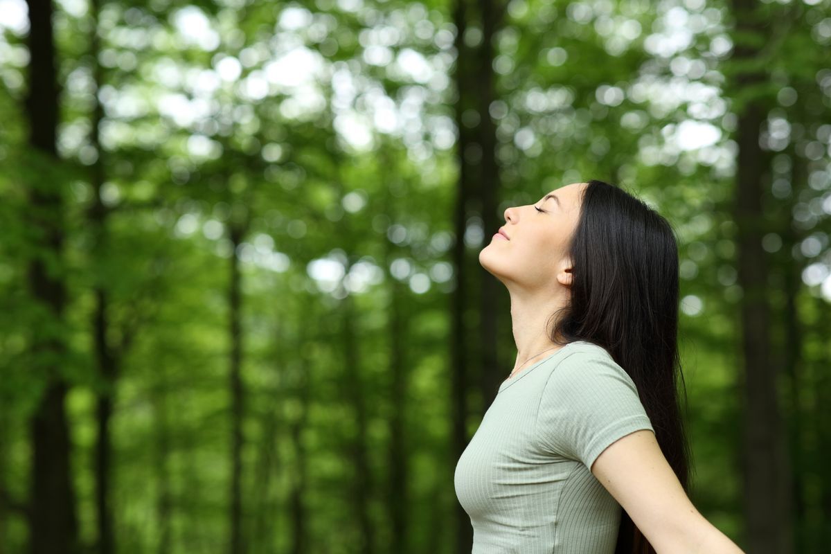 Asian woman feeling rejuvenated while being surrounded by trees 