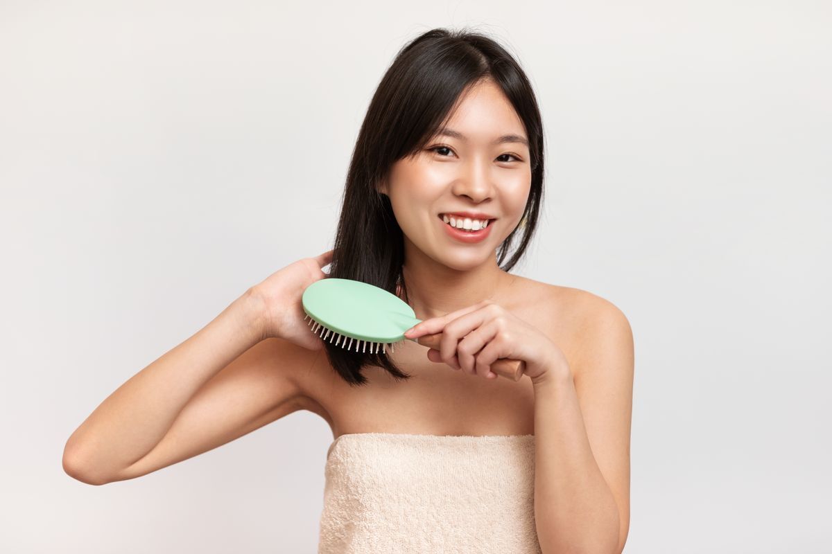 Asian woman using a green paddle brush