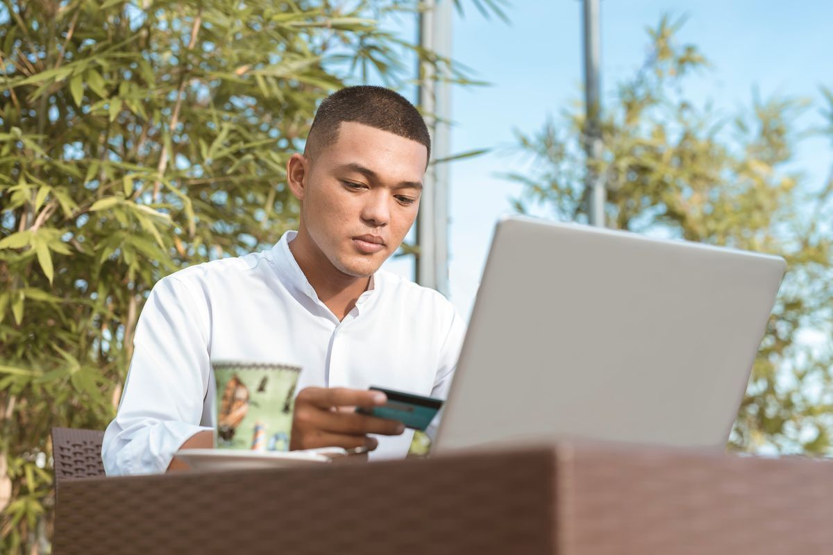 A man working on his laptop while holding a credit card.