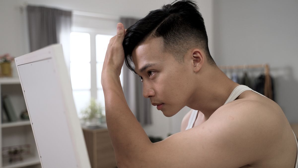 Young man in a white undershirt checking his hair.