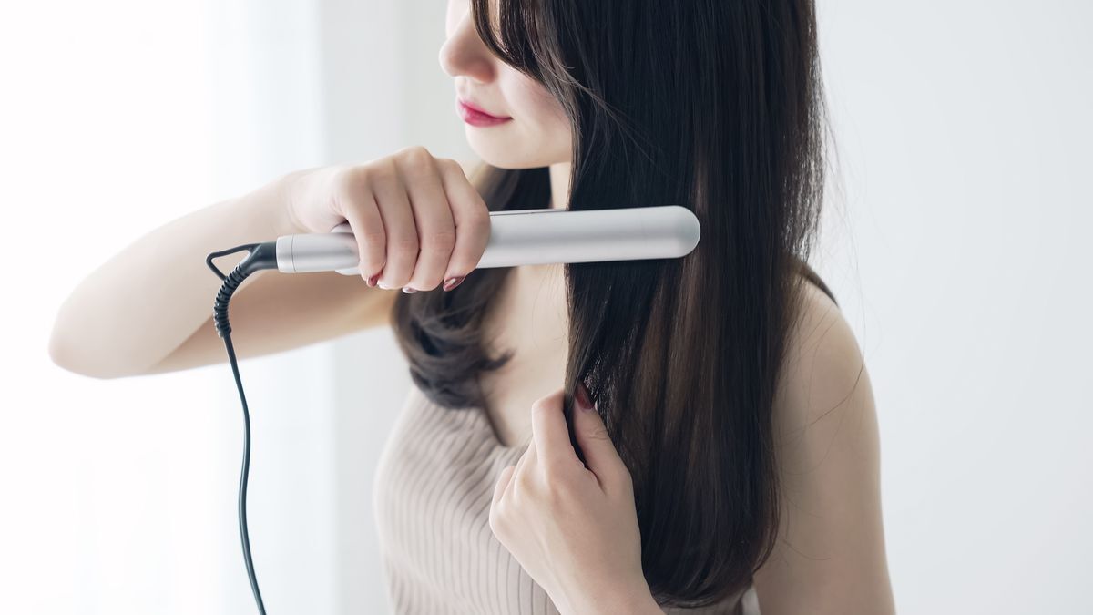 Woman styling her long hair with a hair straightener. 