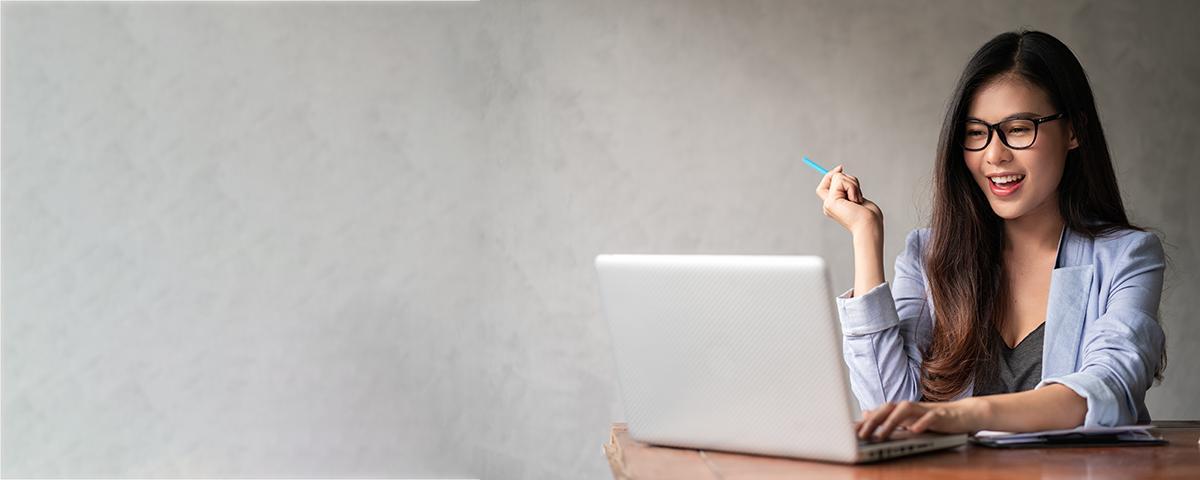 Asian woman with glasses holding pen and looking at laptop