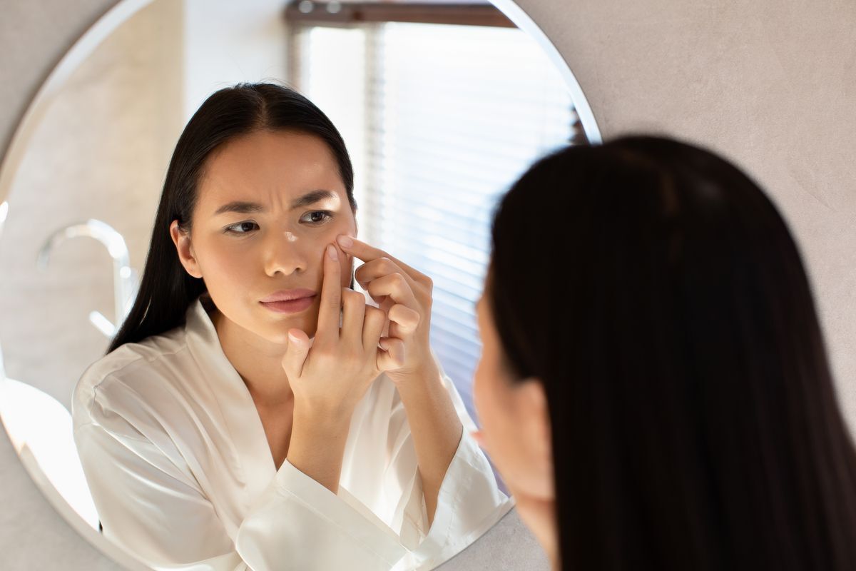 A woman in a white robe pinching her skin in front of the mirror.