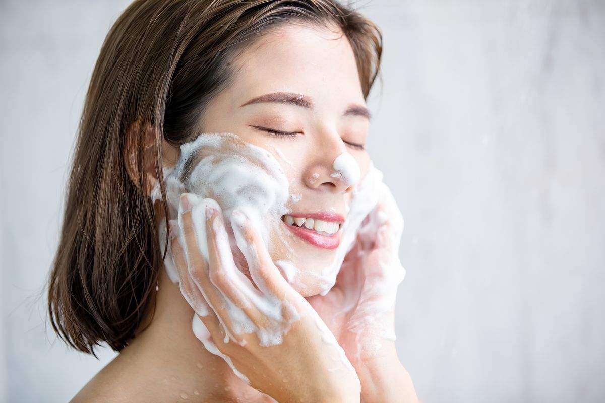 A woman washing her face with a facial foam while smiling.  