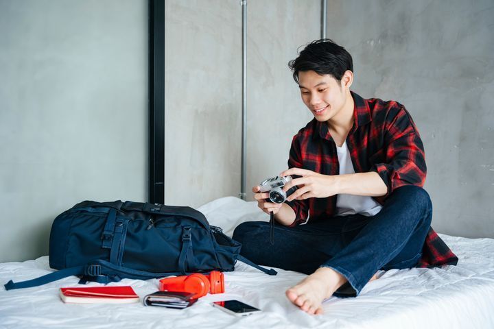 Asian man packing on bed with camera