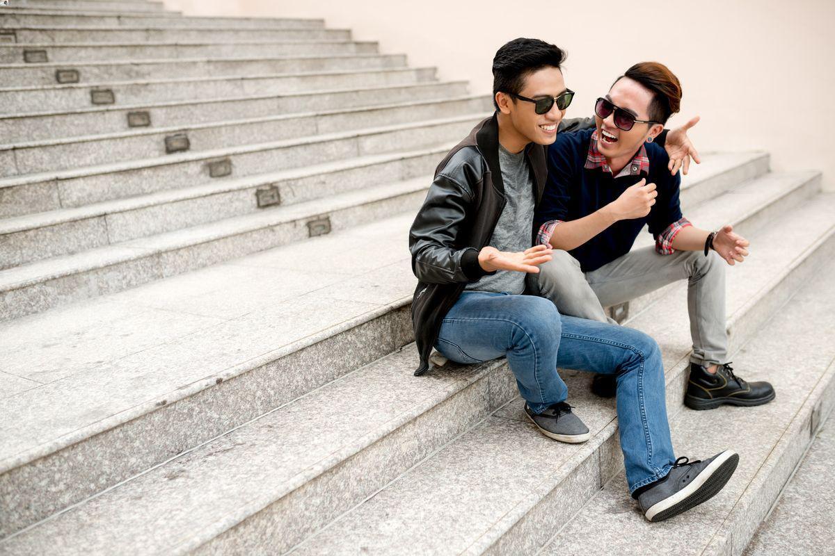 Male friends wearing shades sitting on steps